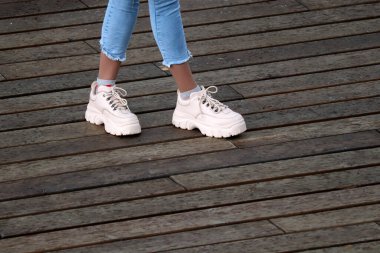 Mavi kotlu kadın bacakları ve yüksek bir platformda beyaz spor ayakkabılar. Sokakta duran kız, gençlik modası, ayakkabı ve giysi konsepti