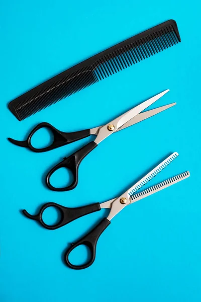 Professional hairdresser scissors and comb on blue background