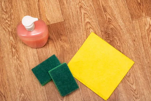 Cleaning agent, sponge and yellow rag on wooden floor top view — Stock Photo, Image