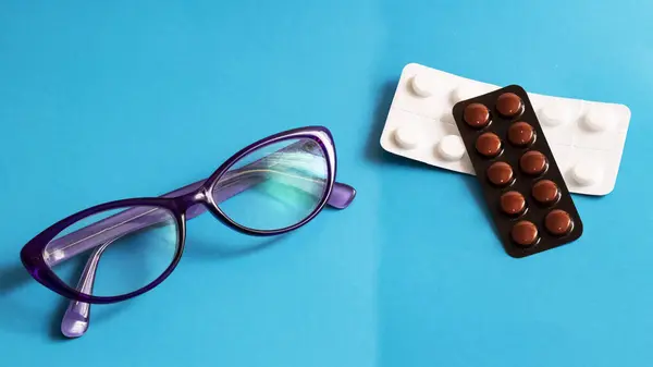 Gafas y paquetes de pastillas sobre un fondo azul — Foto de Stock