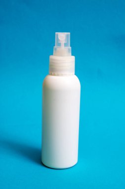 Mavi arka planda beyaz plastik bir dezenfektan şişesi.
