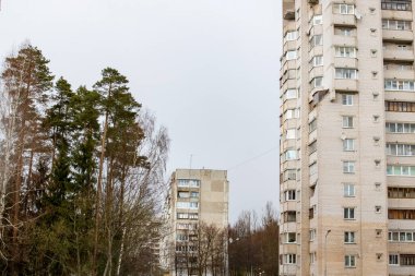Bulutlu gri gökyüzü arka planında uzun apartmanlar ve ağaçlar