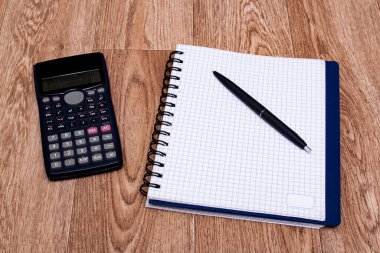 Mühendislik hesap makinesi ve defter ahşap bir masaya yakın.