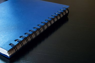 Mavi defter, siyah ahşap bir masada. Yaklaş.