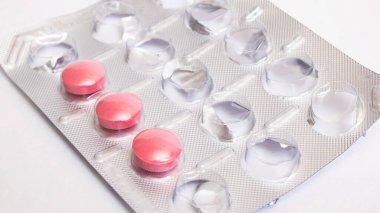 Gri arka planda pakette üç pembe hap. Yakın plan.