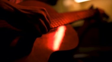 Bir gitarist prova yapıyor. Sönük kırmızı ışıklarla dolu bir odada..