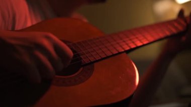 Bir gitarist prova yapıyor. Sönük kırmızı ışıklarla dolu bir odada..