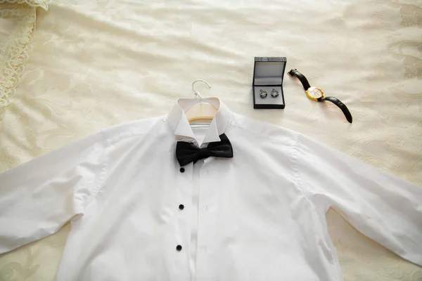 The white shirt, the ring, and the watch of the baby dressing on the bed . Men's classic shirts on the bed .
