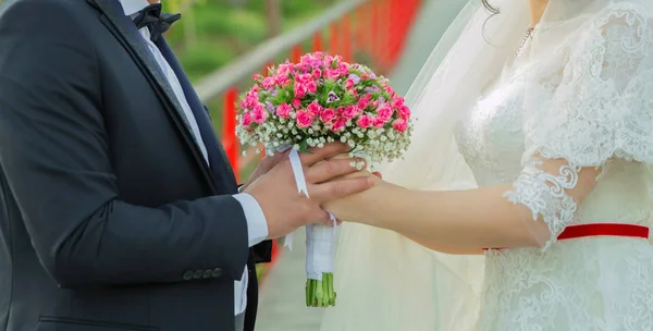 They held the pink flower bouquet in their hands . hands folded behind their back, hold a beautiful little wedding bouquet of roses . The newlyweds hold in their hands a wedding bouquet between each o — Stock Photo, Image