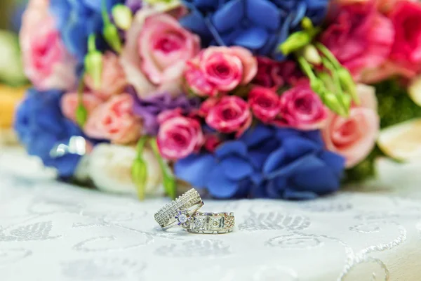 Los hombres y los anillos de novia están en el fondo de un ramo de boda multicolor. Atributos del día de boda. Hermoso ramo nupcial de flores coloridas y rosadas, enfoque selectivo . — Foto de Stock