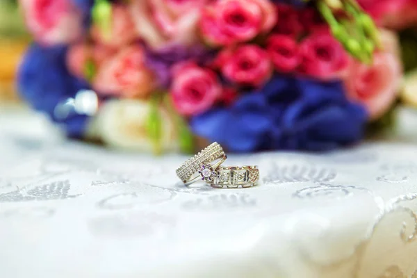 Uomini e anelli nuziali sono sullo sfondo di un bouquet da sposa multicolore. Attributi del giorno del matrimonio. Bellissimo bouquet da sposa di fiori colorati e rosa, fuoco selettivo . — Foto Stock