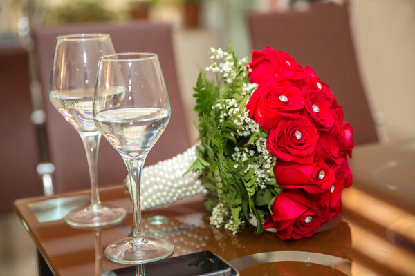 A red wedding bouquet of flowers. Wedding bouquet of red roses and two champagne glasses standing on the authentic . Background with glasses and flowers .