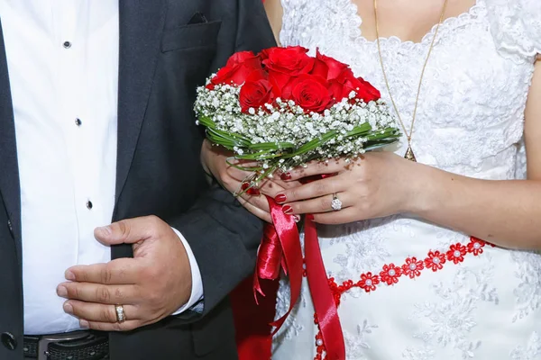 Bride holding colorful flowers bouquet with her hands on wedding day . Wedding. The guy and the girl in a white dress standing and holding in her hands a bouquet of red, white flowers and greenery