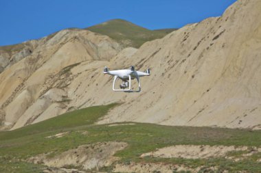 Drone dört helikopter gökyüzü üzerinde yüksek çözünürlüklü dijital kamera ile. Beyaz drone ile dijital fotoğraf makinesi dağ Drone ile yüksek çözünürlüklü dijital fotoğraf makinesi üzerinde gökyüzünde uçan.