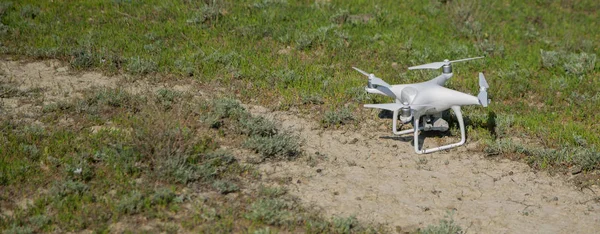 Белый дрон с цифровой камерой, летающей в небе над горным дроном с цифровой камерой высокого разрешения. Дрон с камерой в траве готовится к полету. Летающий беспилотник с голубым небом — стоковое фото