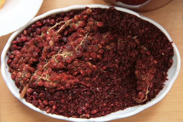 Dried sumac seasoning in a wooden bowl, top view. a handful of red sumac powder in a plate abstract background . Sumak grains and powder . Sumac is in a white plate . — Stock Photo, Image