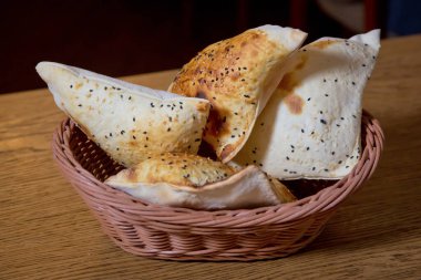 Hasır sepetin ahşap arka planında taze pişmiş ekmeğin yüksek açılı görüntüsü. Tahta masada ekmek sepeti. Ahşap masada çeşitli pişirme ürünleri içeren kompozisyon .