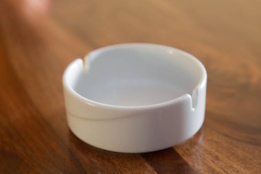 Yaklaş, seçici odaklan, yüzeysel görüş derinliği. Ahşap arka planda izole edilmiş yuvarlak cam kül tablası. Parktaki eski ahşap bir masanın üzerindeki boş yuvarlak cam küllüğü temizle..