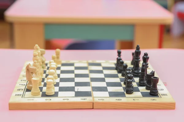 Wooden chess pieces on the chessboard. Intellectual game . Wooden chess pieces and chess clock on a pink background. — Stock Photo, Image