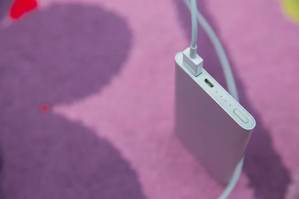 Энергетический банк. Зарядка смартфона серебристым Power Bank через спиральный кабель USB. Зарядка смартфона на розовом ковре  . — стоковое фото