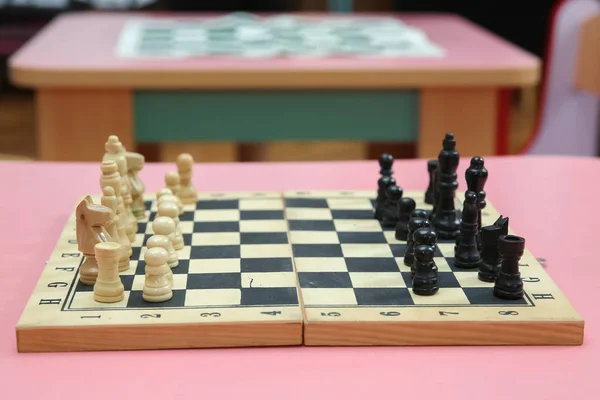 Piezas de ajedrez de madera en el tablero de ajedrez. Juego intelectual. Piezas de ajedrez de madera y reloj de ajedrez sobre fondo rosa . — Foto de Stock