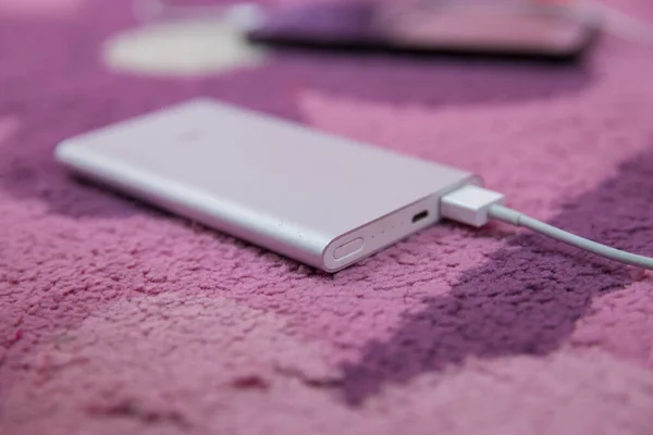 Carga de Smartphone con banco de energía plateado a través del cable USB espiral. Carga de Smartphone con banco de energía en alfombra rosa. Banco de energía  . — Foto de Stock