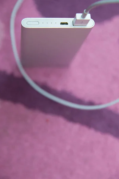 Banco de energía. Carga de Smartphone con banco de energía plateado a través del cable USB espiral. Carga de Smartphone con banco de energía en alfombra rosa  . — Foto de Stock