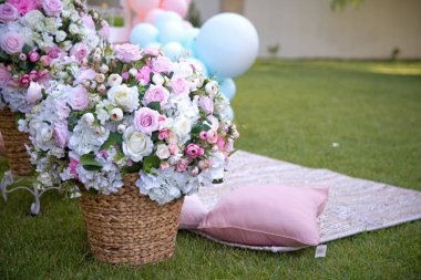 Pembe ve beyaz çiçek sepeti yeşil çimen bahçesi yazı. Bahçede yaz pikniği. Mavi balon. Çimlerin üzerinde beyaz çiçekler olan piknik sepeti. .
