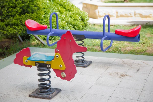 Zaaien op kinderspeelplaats in park. kinderen paardrijden in de speeltuin schommelen op een metalen spiraal. Voorjaarspaard in de speeltuin. — Stockfoto