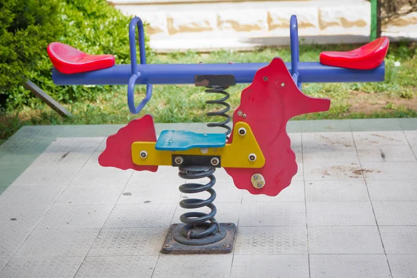 Zaaien op kinderspeelplaats in park. kinderen paardrijden in de speeltuin schommelen op een metalen spiraal. Voorjaarspaard in de speeltuin. — Stockfoto