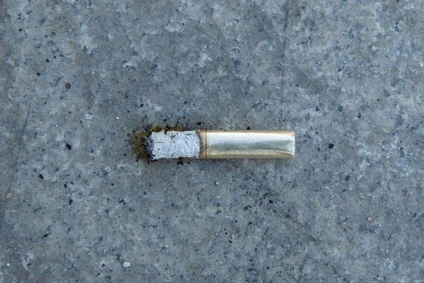 Cigarettes in gold . cigarette end on the pavement . Discarded cigarette on the street. Environmental pollution. Cigarette butts on the road . Smoke and ashes on the pavement.