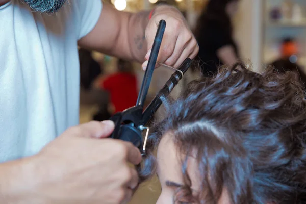 hairdresser straightening hair over . blonde doing the Curling irons in the beauty salon . Professional hairdresser . Close up of stylist\'s hand using curling iron working for woman client hair .