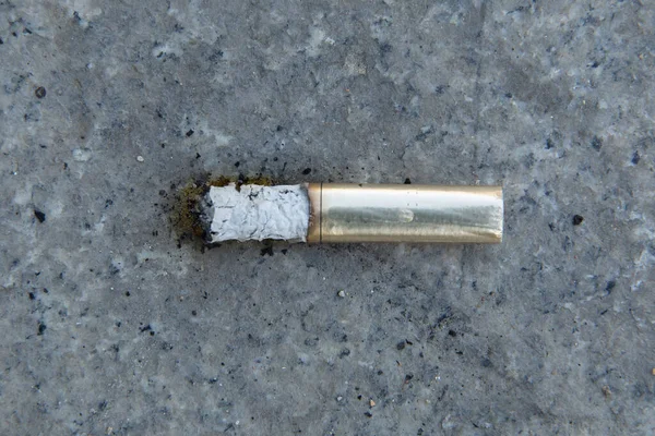Cigarettes in gold . cigarette end on the pavement . Discarded cigarette on the street. Environmental pollution. Cigarette butts on the road . Smoke and ashes on the pavement.