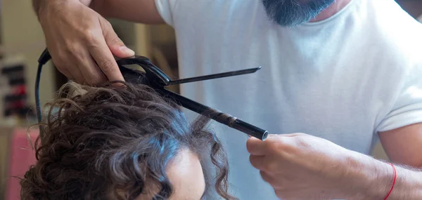 hairdresser straightening hair over . blonde doing the Curling irons in the beauty salon . Professional hairdresser . Close up of stylist\'s hand using curling iron working for woman client hair .
