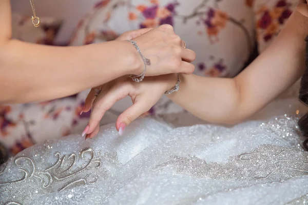 Невеста надевает украшения, фокусируется на браслете. Крупным планом жениха, дарящего невесте браслет, как символ его любви в день их свадьбы. Подружка невесты помогает надеть ему на руку браслет для невесты . — стоковое фото