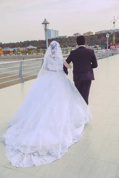 Close up photo of long wonderful skirts of the bride. back view of newlyweds walking along the road . back view of bride in long wedding dress. — 图库照片