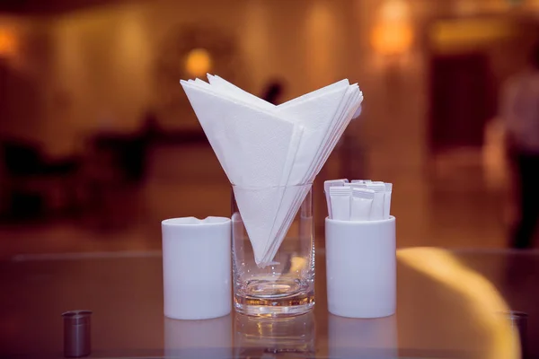 Weiße Servietten in einem Metallserviettenhalter, Gewürze Salz und Pfeffer auf einem Holzglastisch, Panoramablick. Zahnstocher. ein Tisch in einem Café oder Restaurant. — Stockfoto