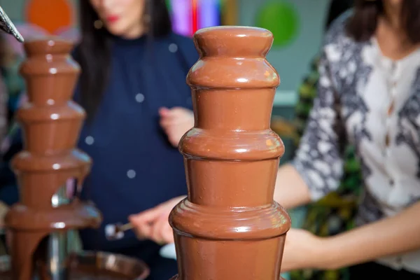 Chocolate fountain with fruits. Children birthday party . Homemade chocolate fountain fondue with marshmallow on a skewer dripping in chocolate sauce on blurred background and copy space .