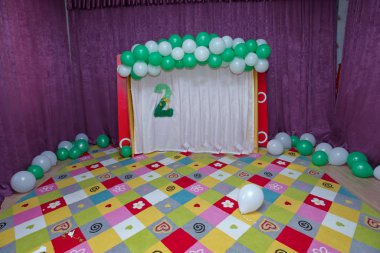 Renkli bebek halısı. Beyaz ve yeşil balonlar. Pembe perde. Yeşil suni çiçekli iki yazı. 2 Yaş Dekorasyonu.