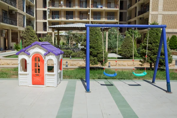 Entertainment area.kids playhouse in the entertainment center. Plastic children play house . Childs swing in a park .Plastic and Empty blue and green chain swings in children . plastic colorful house