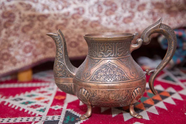 Vintage oriental teapot on a background of carpet .Beautiful vintage copper teapot kettle with tarnished metal, sitting background of carpet. Old teapot with abrasions. Copper teapot . Copper bowl . — Stock Photo, Image