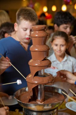 Meyveli çikolata çeşmesi. Çocukların doğum günü partisi. Ev yapımı çikolata çeşmesi fondüsü ve bulanık arka planda çikolata sosu damlayan bir şiş üzerine marshmallow ve fotokopi alanı. .