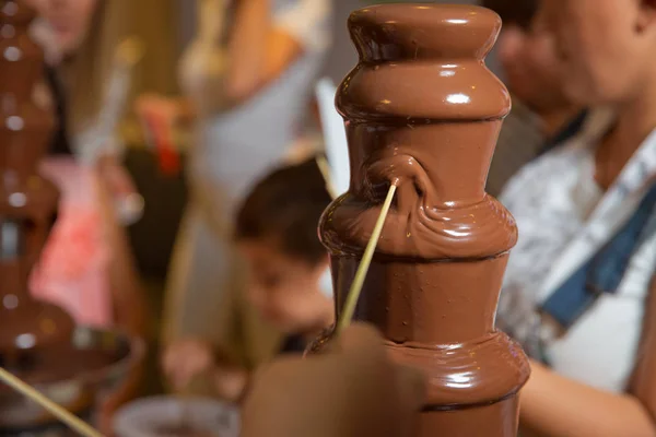 Шоколадный фонтан с фруктами. День рождения детей. Фондю из домашнего шоколада с зефиром на шампуре, капающий в шоколадный соус на размытом фоне и копировальное пространство  . — стоковое фото