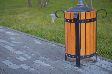 Soldaki boşluğu kopyala. Parkta çöp kutusu var. Tahta bir vazo ve rahat boş bir park tezgahı. Parktaki ahşap bir muhafazanın içindeki sarı çöp kutusu..