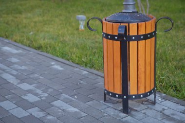 Soldaki boşluğu kopyala. Parkta çöp kutusu var. Tahta bir vazo ve rahat boş bir park tezgahı. Parktaki ahşap bir muhafazanın içindeki sarı çöp kutusu..