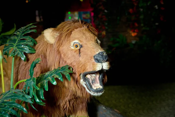Statue lion . Life size replica model . The lion is in an artificial green forest at night . Brown Lion Animal Figure Statue .