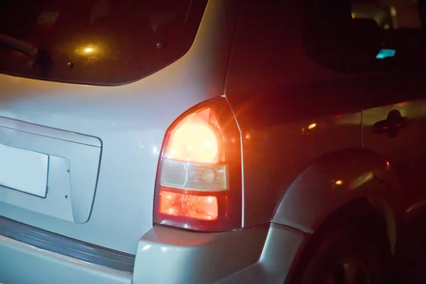 A red light at the rear of a metallic car waiting at crossroad.The rear lights of the car parked at red lights in the evening. Rear view of traffic jams, rush hour . A tail-light of car at night city. — Stok fotoğraf