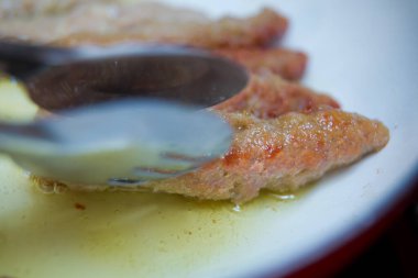 The long cutlet is fried in a red pan. Close up of a woman's hand with a kitchen spatula looks like a frying pan fried cutlets . Juicy homemade cutlets beef, pork, chicken .
