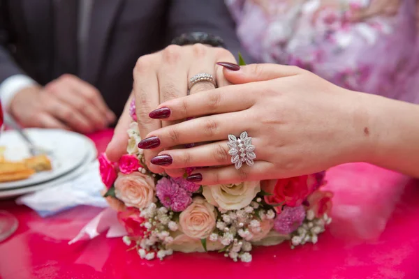 Brud och brudgum med Förlovning guld ringar som läggs på bordet, och bredvid dem ligger en bröllopsbukett. rött bord. Färgglada bröllop blommor . — Stockfoto