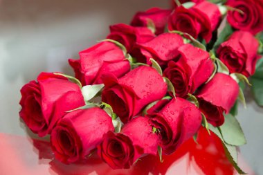 Gelin buketi. Camda, aynada bir düğün buketinin yansıması. Çiçekler masanın üzerinde yatıyor. Cam bir masanın üzerinde gül kolyesi aranjmanı.